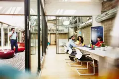 Three colleagues having a meeting in a meeting room, while one colleague is making a call outside the room.
