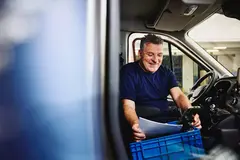 Smiling male sitting in driver's seat of a logistics truck holding papers and a GPS
