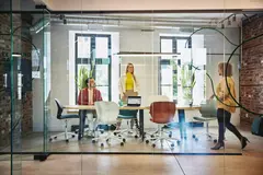 Female and male are sitting and female is standing at a table in a office meeting room