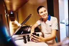 Womale in housekeeping uniform, holding small toiletries bottles.
