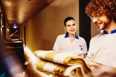 male and female in housekeeping uniform working together. male holding towels.

