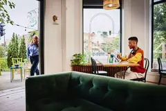 Female entering a cafe, male sitting at a table with headphones working on a tablet with a touch pen