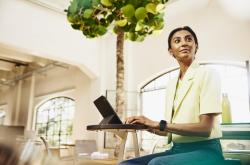 Woman looking away while sitting at table working on a tablet.