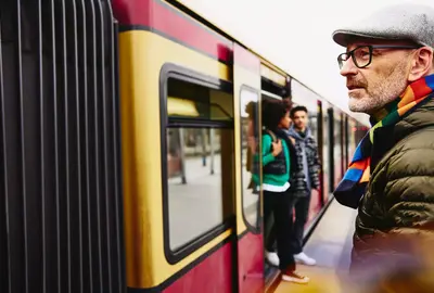 male standing next to a train. Two people getting out of a train in the background.
