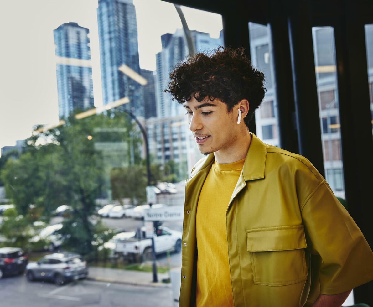 Male in yellow shirt, width earphones, standing at a window looking down Male in yellow shirt, width earphones, standing at a window looking down