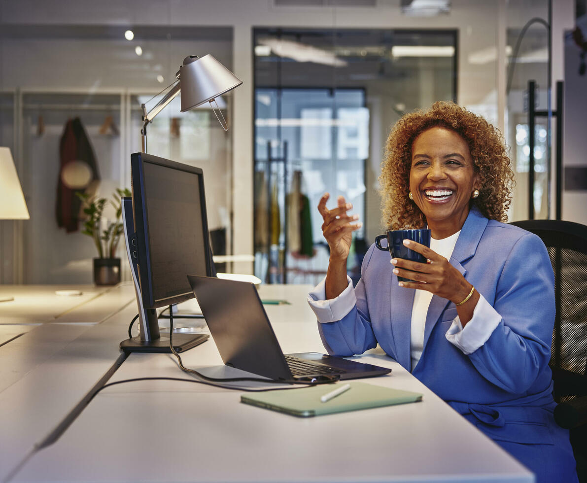Female with blue blazer sitting behind computer at a desk, smiling to a person Female with blue blazer sitting behind computer at a desk, smiling to a person