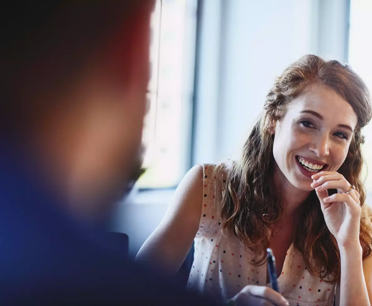 Womale smiling at a colleague holding a pen.Randstad Human Forward