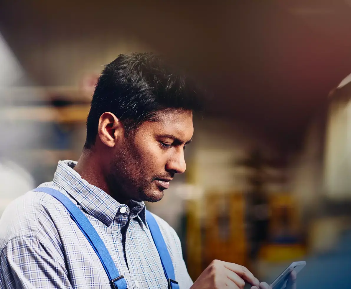Focused male looking down to phone in production site.
