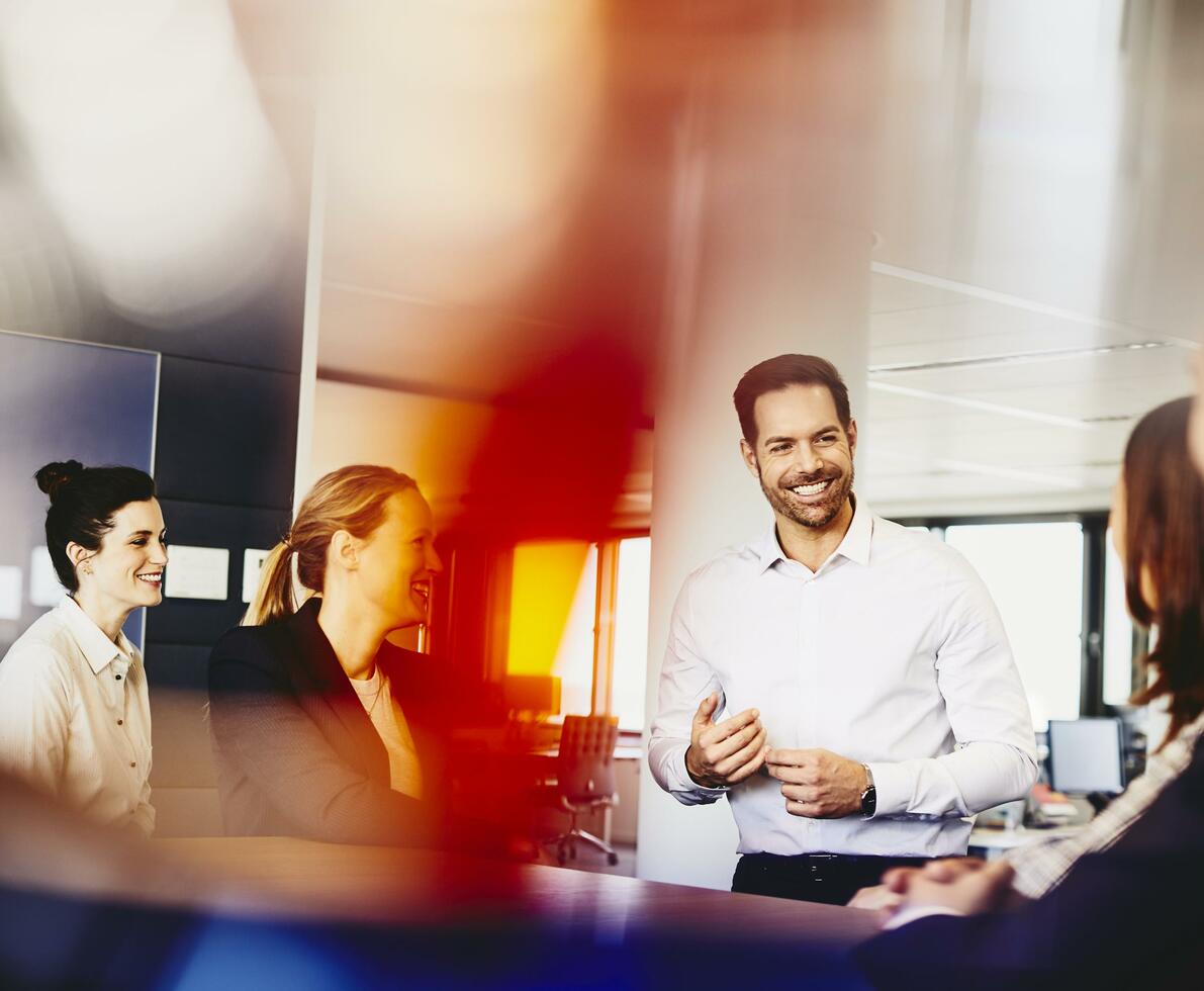 Business men and women in an office having a meeting. Primary color: red.