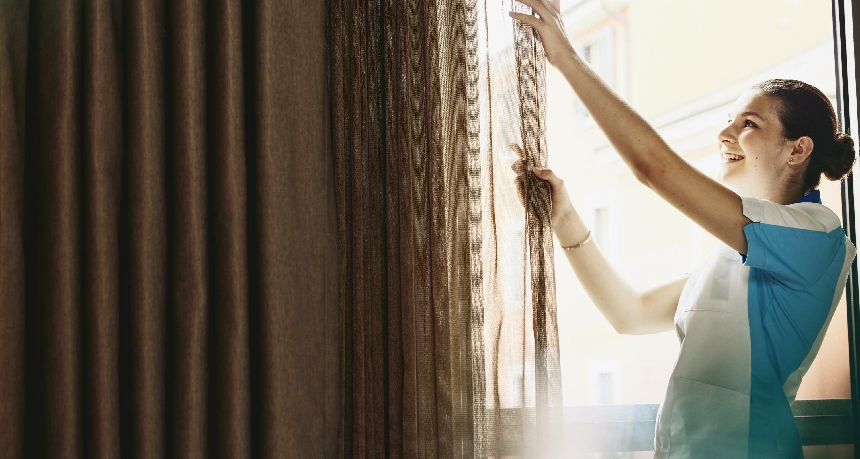Smiling woman closing/opening curtains in a hotel room.