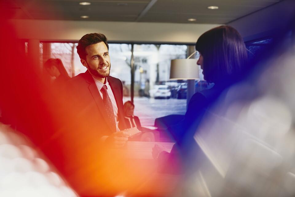 Business man receiving an entrance pass at a reception desk. Primary color: red.