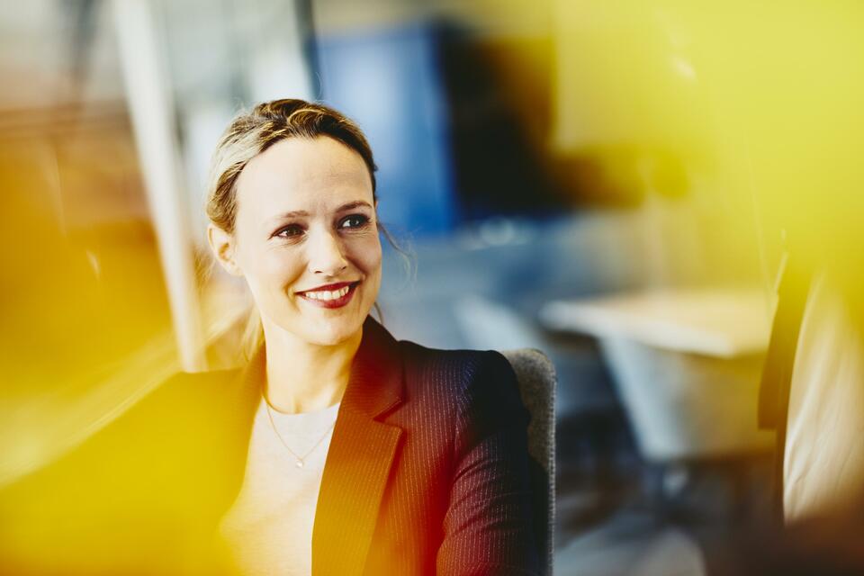 Woman in suit in an office smiling. Primary color: yellow.