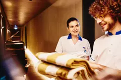male and female in housekeeping uniform working together. male holding towels.
